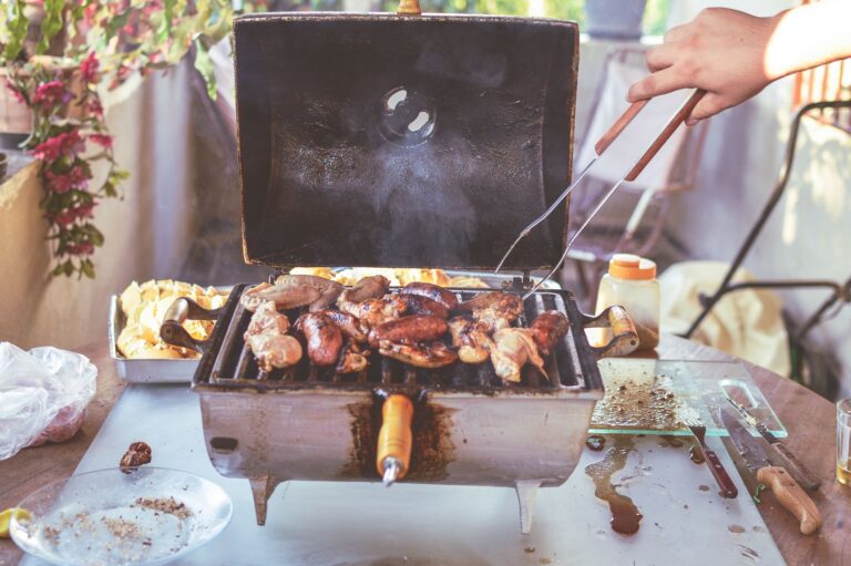 Grătar cu cărbune într-o curte, cu bucăți de carne și legume colorate care se rumenesc pe grilaj